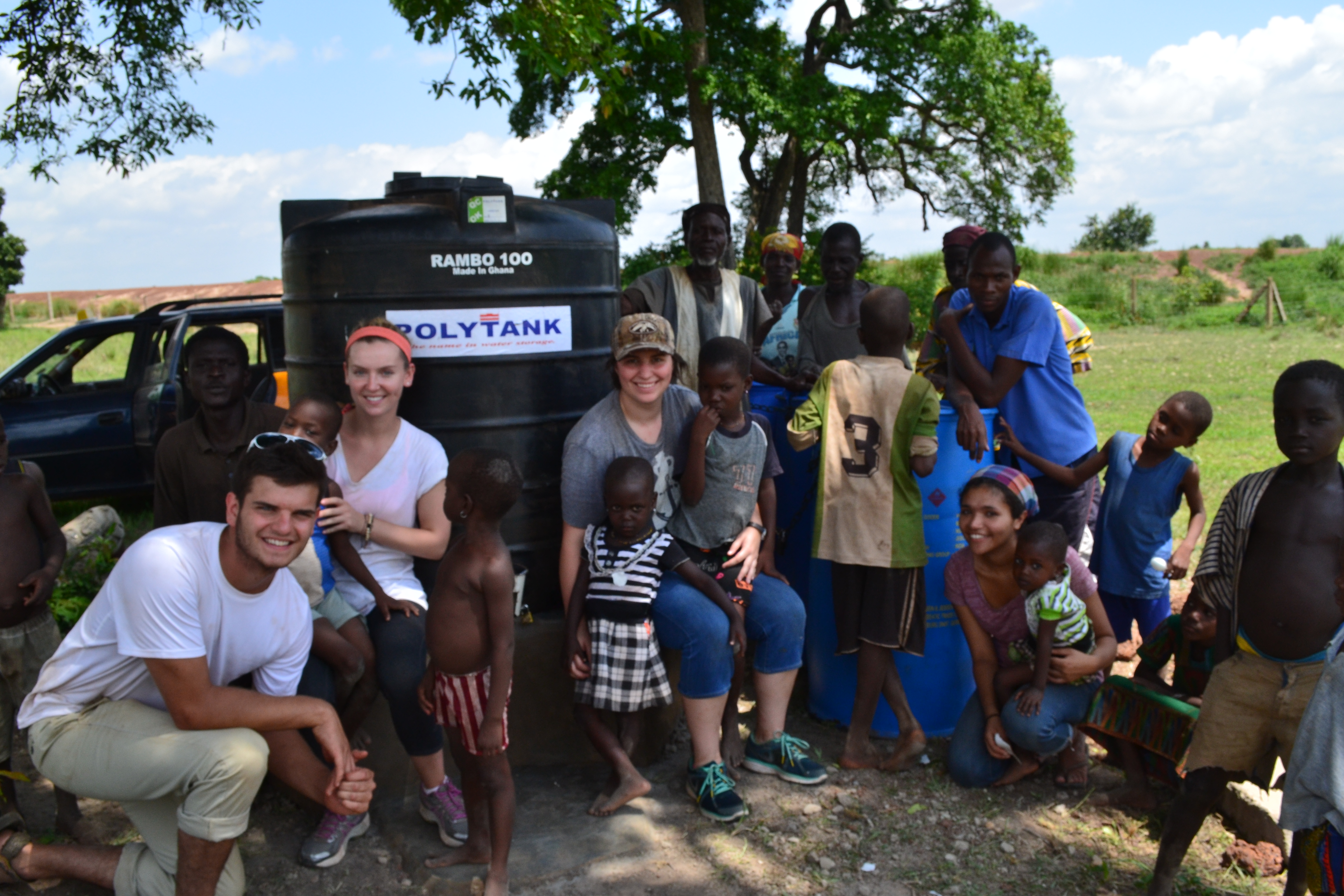 Team Sharifa (Katie, Lucas, Stephanie & Sandra) post with their women entrepenuers and some kiddos in front of Namdu's up and running water treatment center